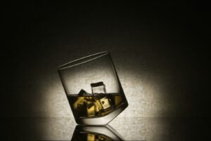 A glass of whiskey with ice cubes on a reflective surface