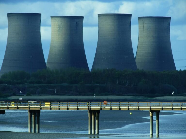 View of industrial cooling towers and a bridge over water, showcasing energy infrastructure.