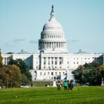 a large white building with a dome and a green lawn in front with United States Capitol in the background