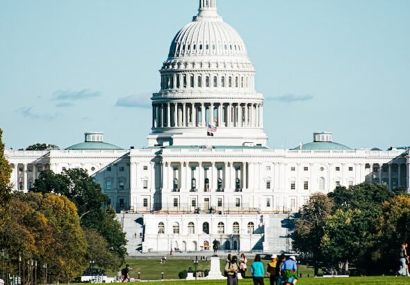 a large white building with a dome and a green lawn in front with United States Capitol in the background