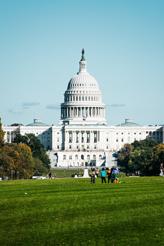 a large white building with a dome and a green lawn in front with United States Capitol in the background, White House
