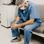 A male doctor in hospital attire sitting pensively, representing healthcare challenges, fraud, doctor, surgeon,