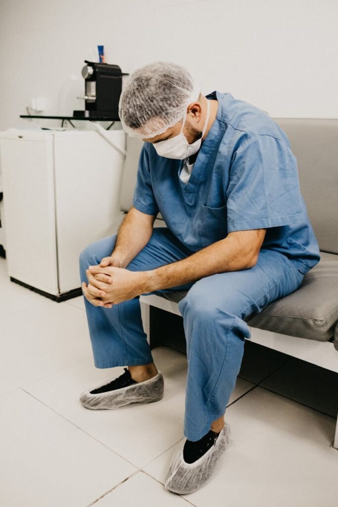 A male doctor in hospital attire sitting pensively, representing healthcare challenges, fraud, doctor, surgeon,