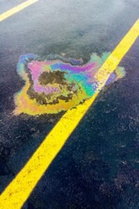Vibrant rainbow-colored oil spill on black asphalt with yellow lines in a parking lot.