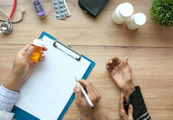 A doctor holds a pill bottle while consulting with an elderly patient. A stethoscope and prescriptions are visible. medicaid, medicare, health