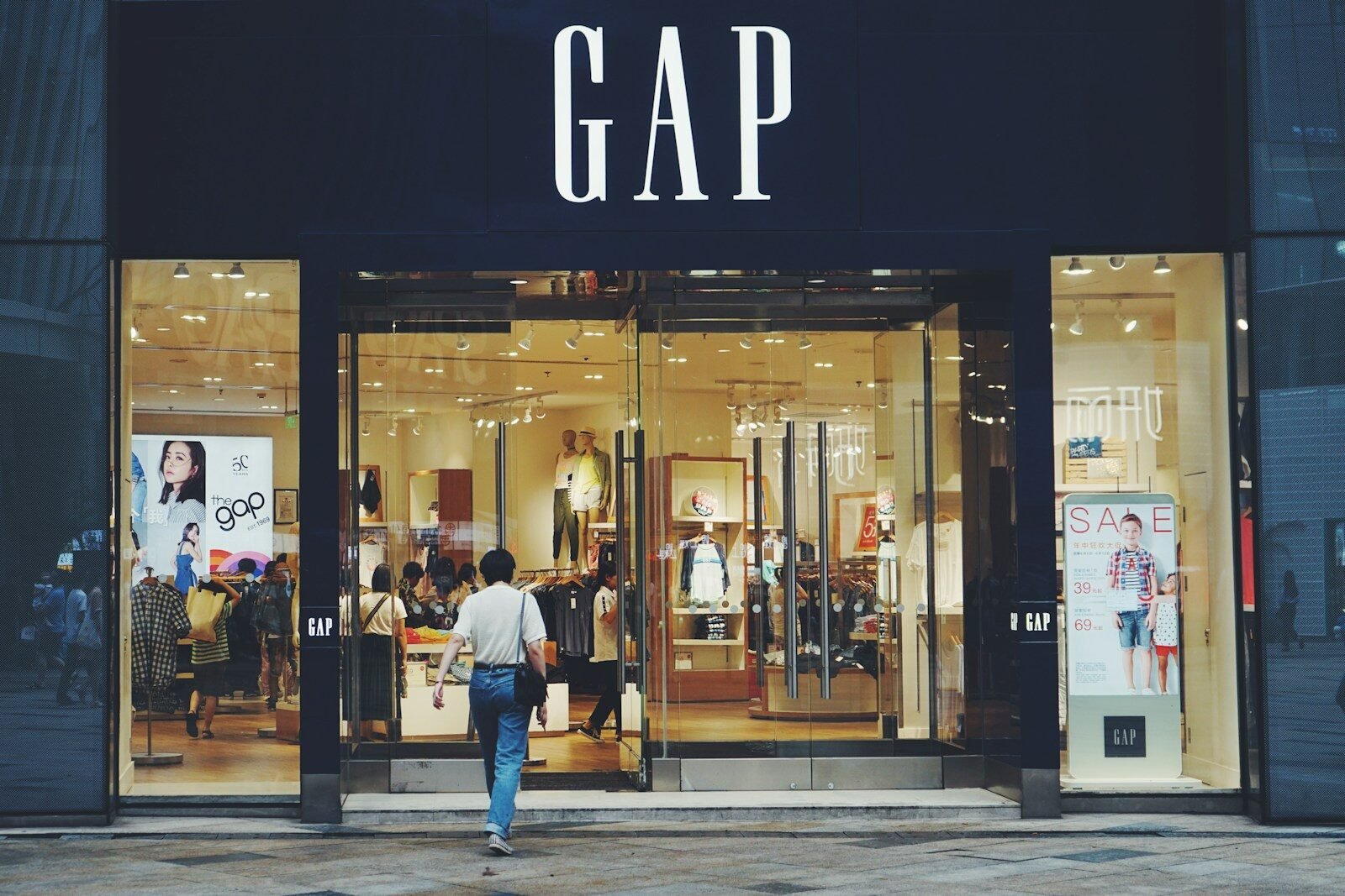 person in white shirt and blue jeans walking inside GAP store, gap