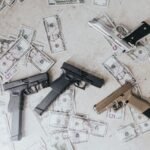 Multiple firearms and US dollar bills scattered on a floor in a high-angle view.