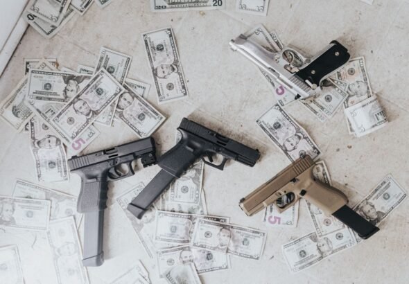 Multiple firearms and US dollar bills scattered on a floor in a high-angle view.